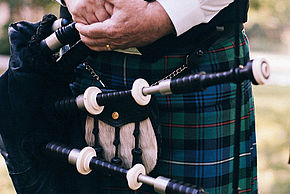Photo d'une cornemuse dans les mains d'un musicien portant un kilt