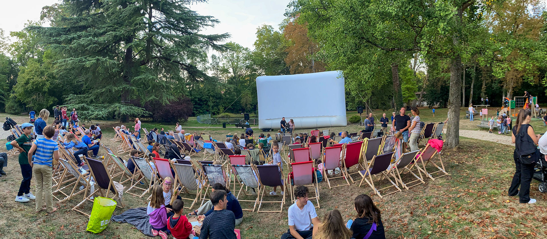 Photo du ciné plein air 2022 avec le public assis dans des transats devant un écran de cinéma dans le parc de la Baronnie de Seine-Port
