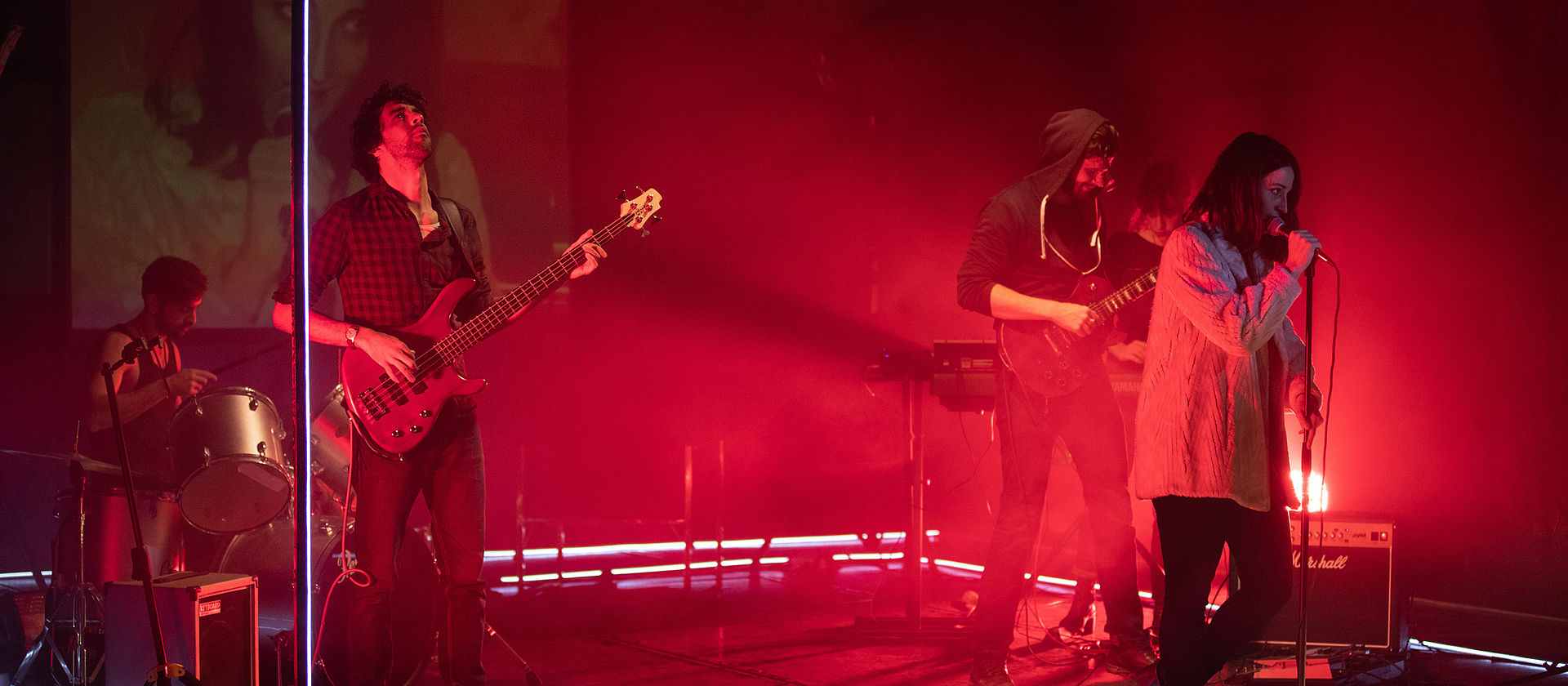 Photo d'un concert avec une chanteuse, un bassiste, un guitariste et un batteur sur scène, lumière rouge